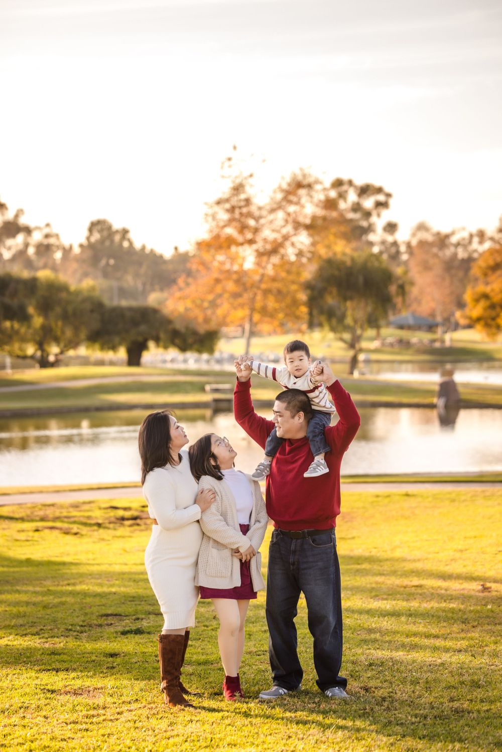 A family enjoys a golden sunset moment together in a park with autumn trees and a lake in the background.