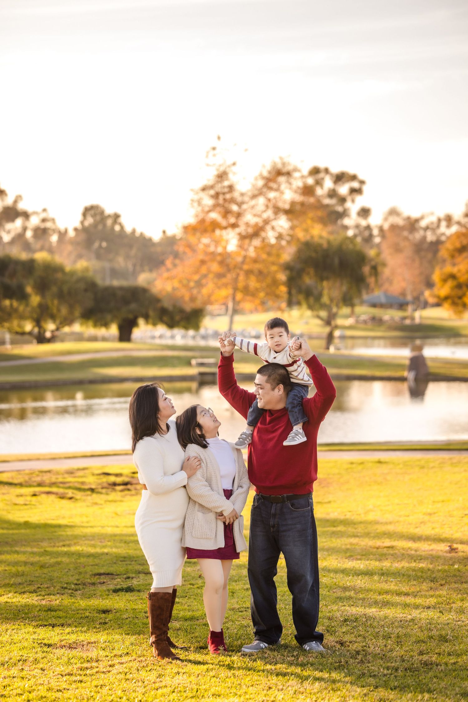 A family enjoys a golden sunset moment together in a park with autumn trees and a lake in the background.