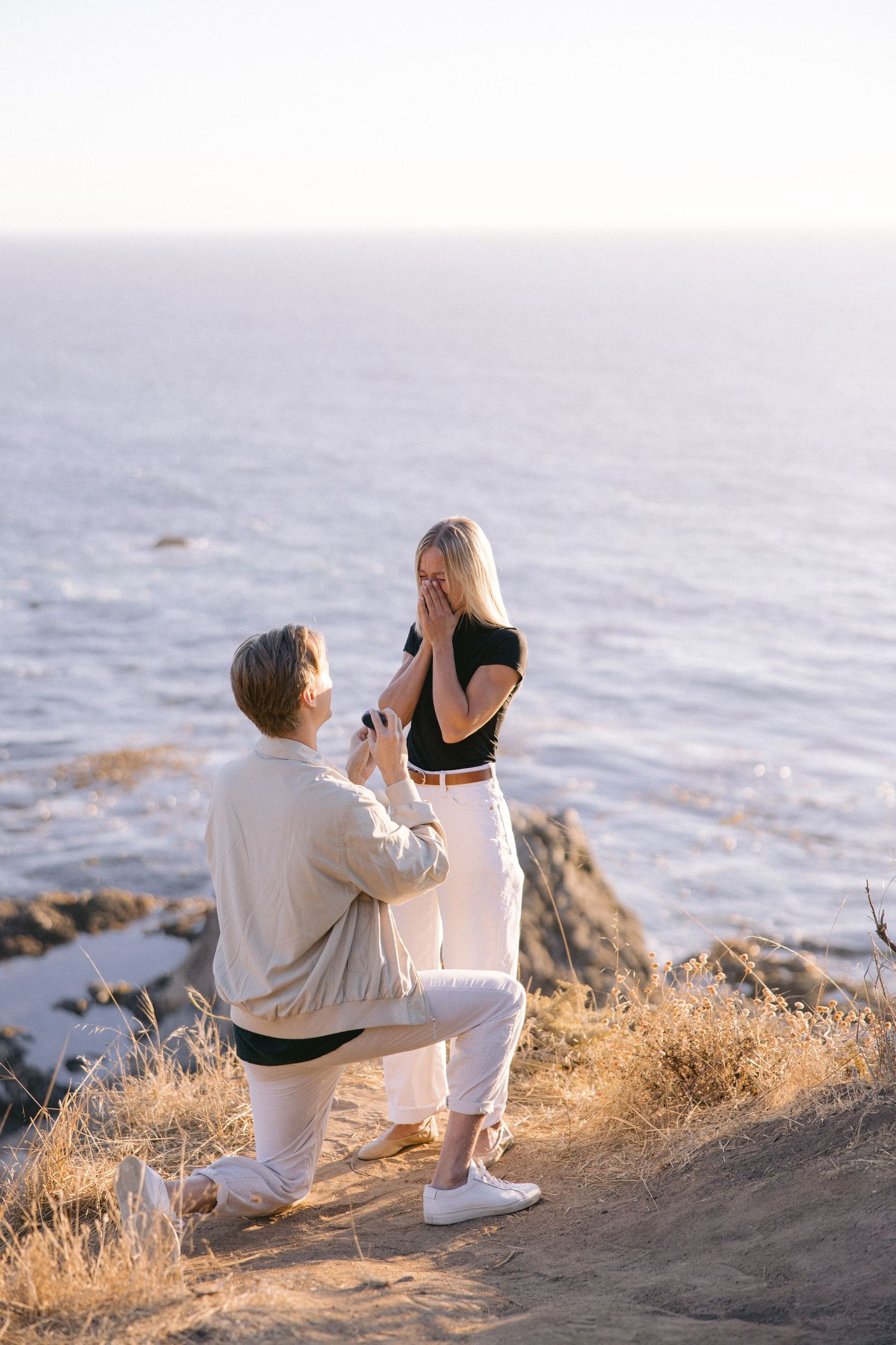 Romantic seaside proposal moment on a coastal cliff during golden hour.