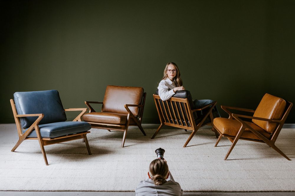 A collection of mid-century modern lounge chairs in leather and wood arranged in a semicircle on a light carpet.
