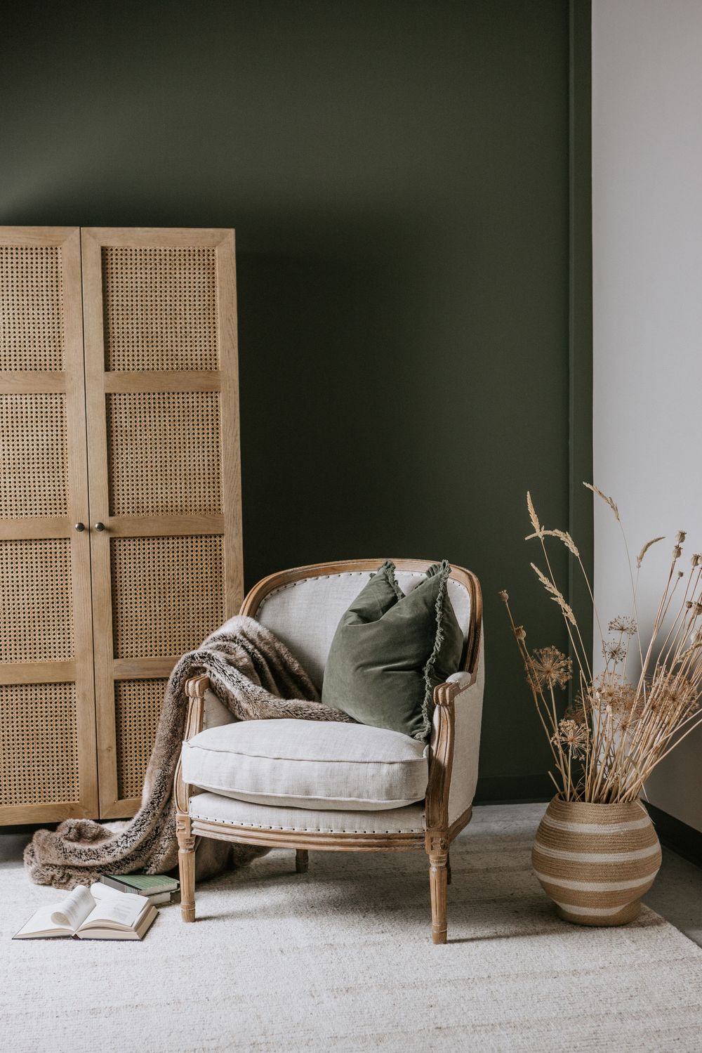A serene living room corner featuring a rattan daybed with green cushions and natural decor against a dark green wall.