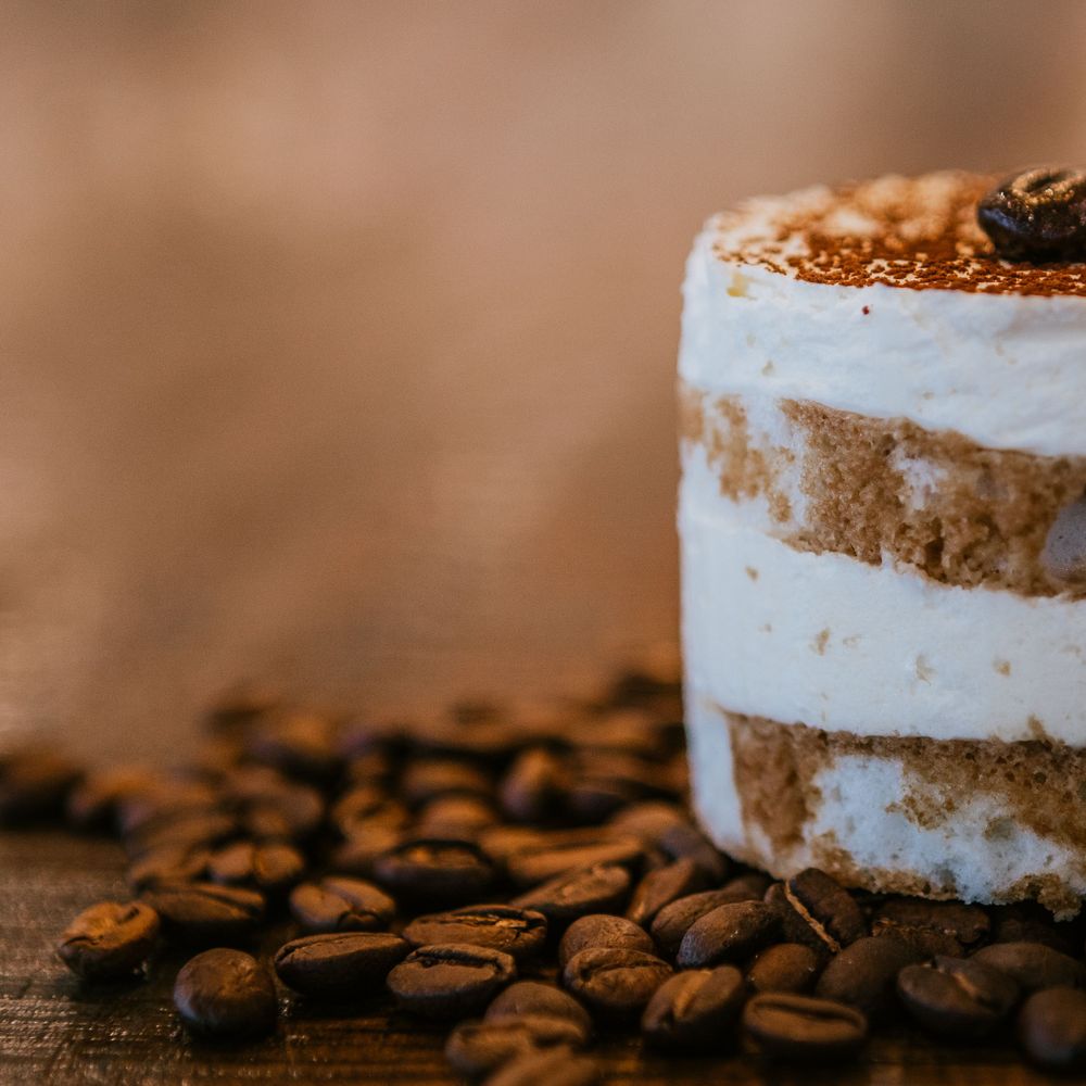 Coffee tiramisu dessert with coffee beans scattered around on wooden surface.