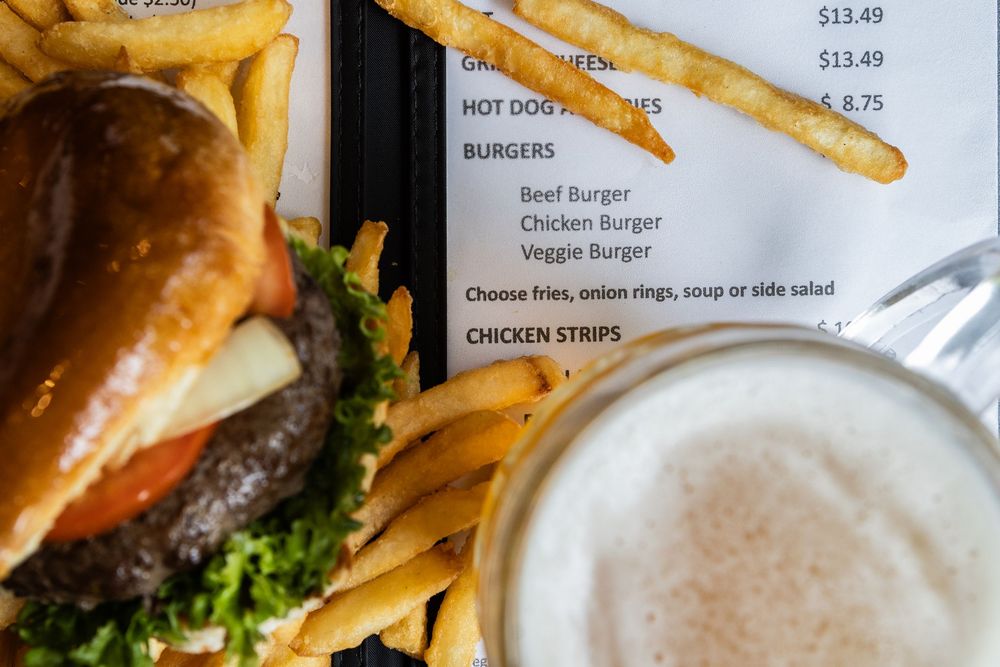 A juicy burger with lettuce alongside golden french fries and a frothy beer, with a menu visible in the background.