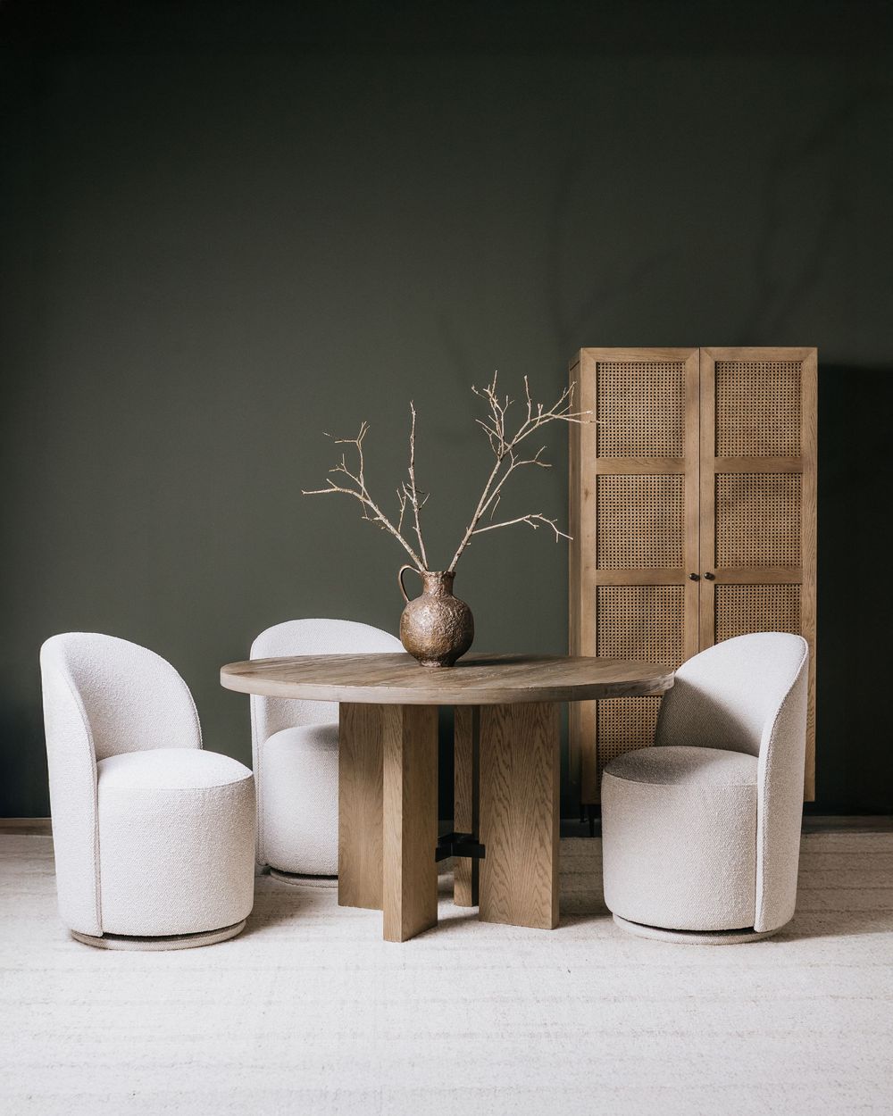 Modern minimalist furniture arrangement with wooden table and white curved chairs against dark wall with decorative vase.