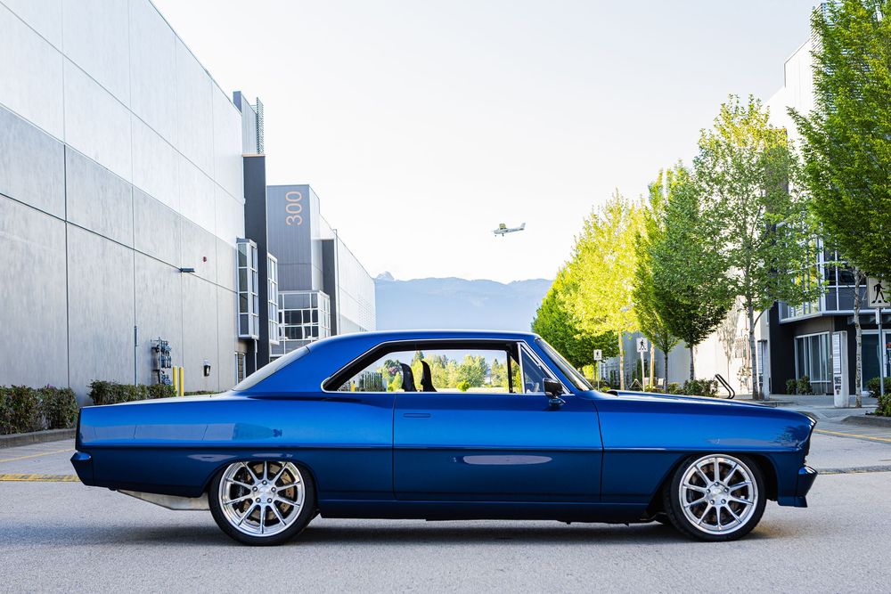 A sleek blue custom car with chrome wheels sits low to the ground against an industrial backdrop.