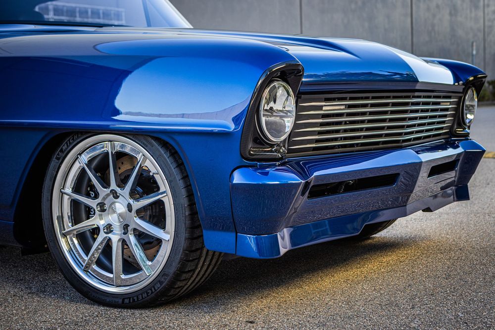 A bright blue classic car with chrome trim and custom wheels photographed from multiple low angles against a concrete wall.