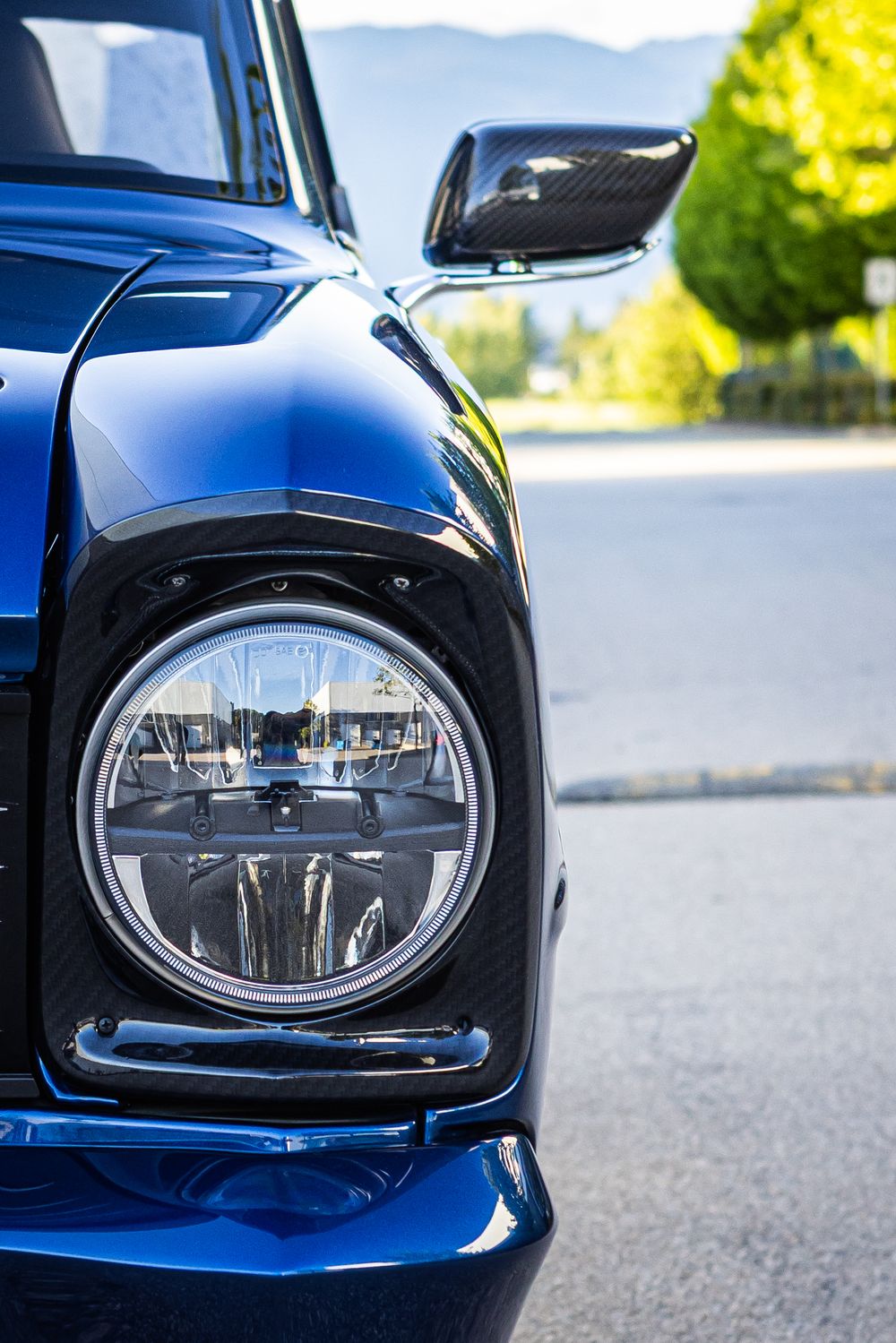 Close-up view of a classic blue Mini Cooper's round LED headlight and front quarter panel detail.