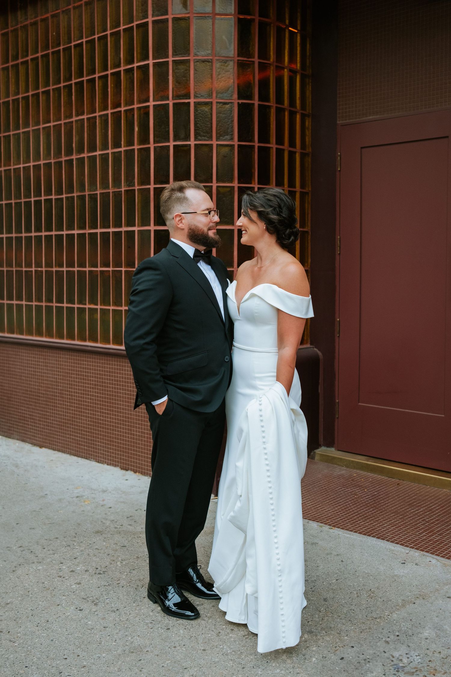 Elegant wedding couple shares intimate moment against brick wall with metal grating.