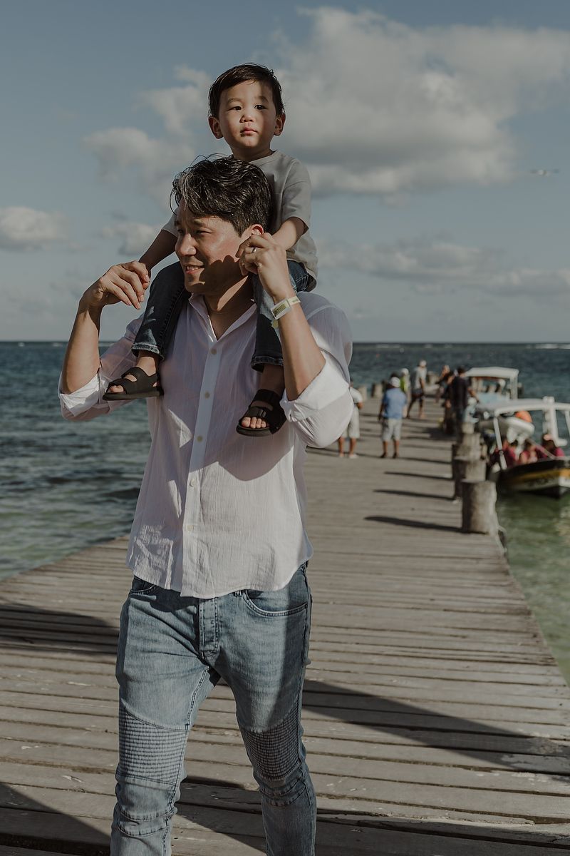 Father carrying son on shoulders during maternity family session on pier in Puerto Morelos.