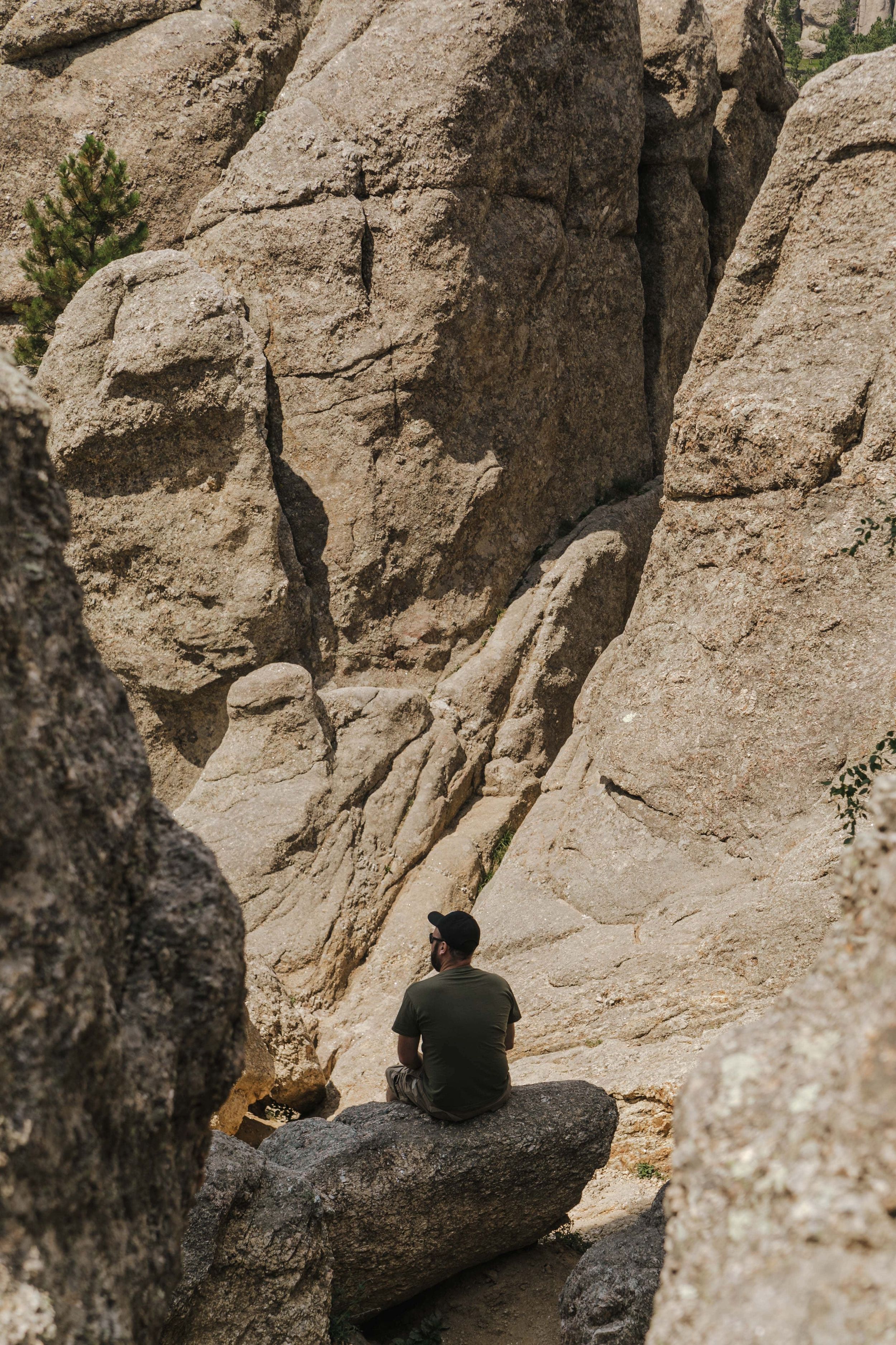 A person sits alone on a rocky outcrop surrounded by tall granite cliffs in a natural climbing area.