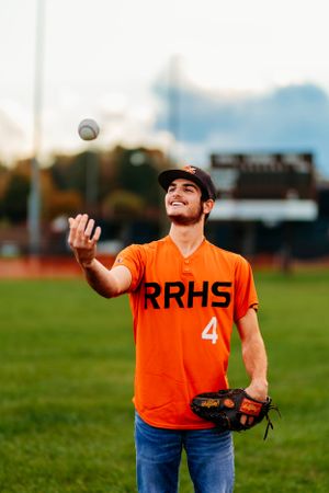 RRHS #4 baseball player in orange jersey tossing a ball while wearing a fielding glove.