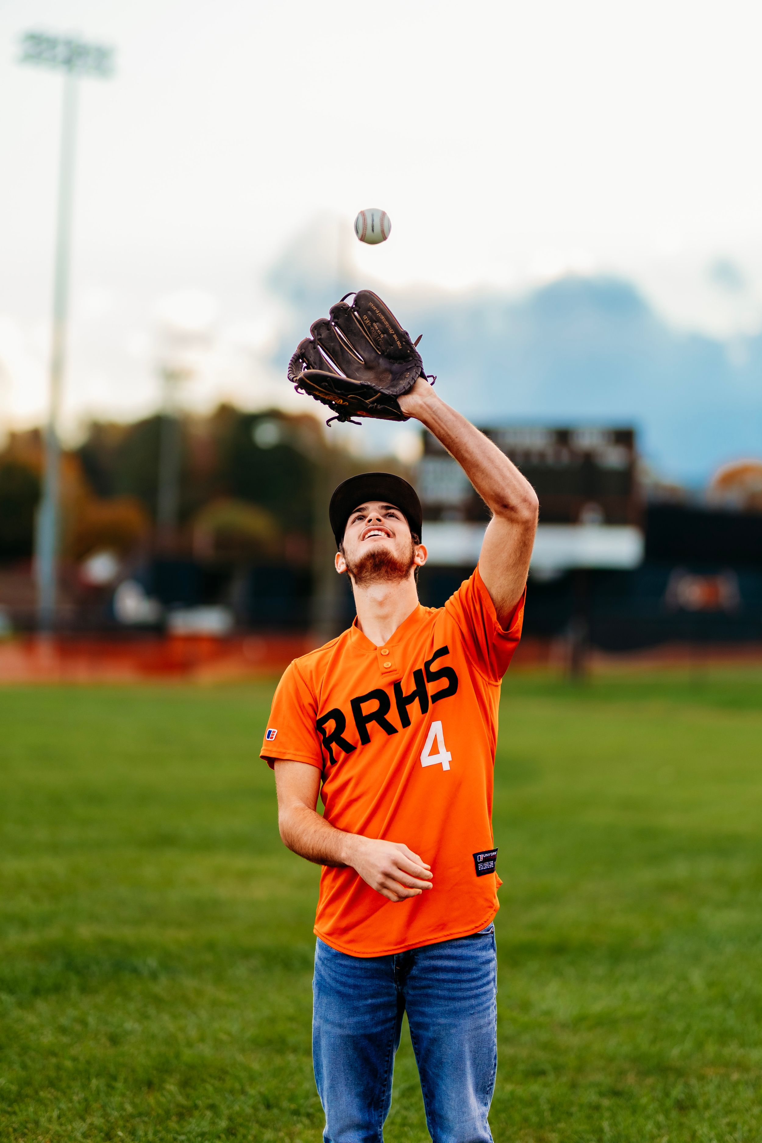 RRHS #4 baseball player in orange jersey catching a ball with glove raised overhead on field.