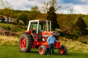 Farmer in blue shirt posing beside a classic red International tractor on green farmland.