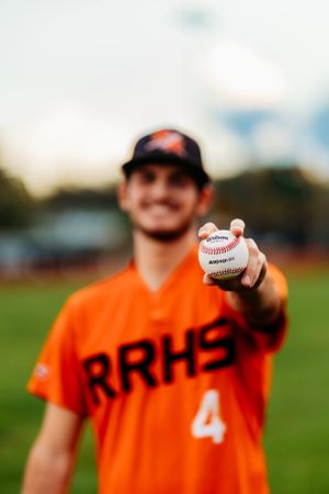 RRHS baseball player number 4 holding a Wilson baseball toward camera on the field.