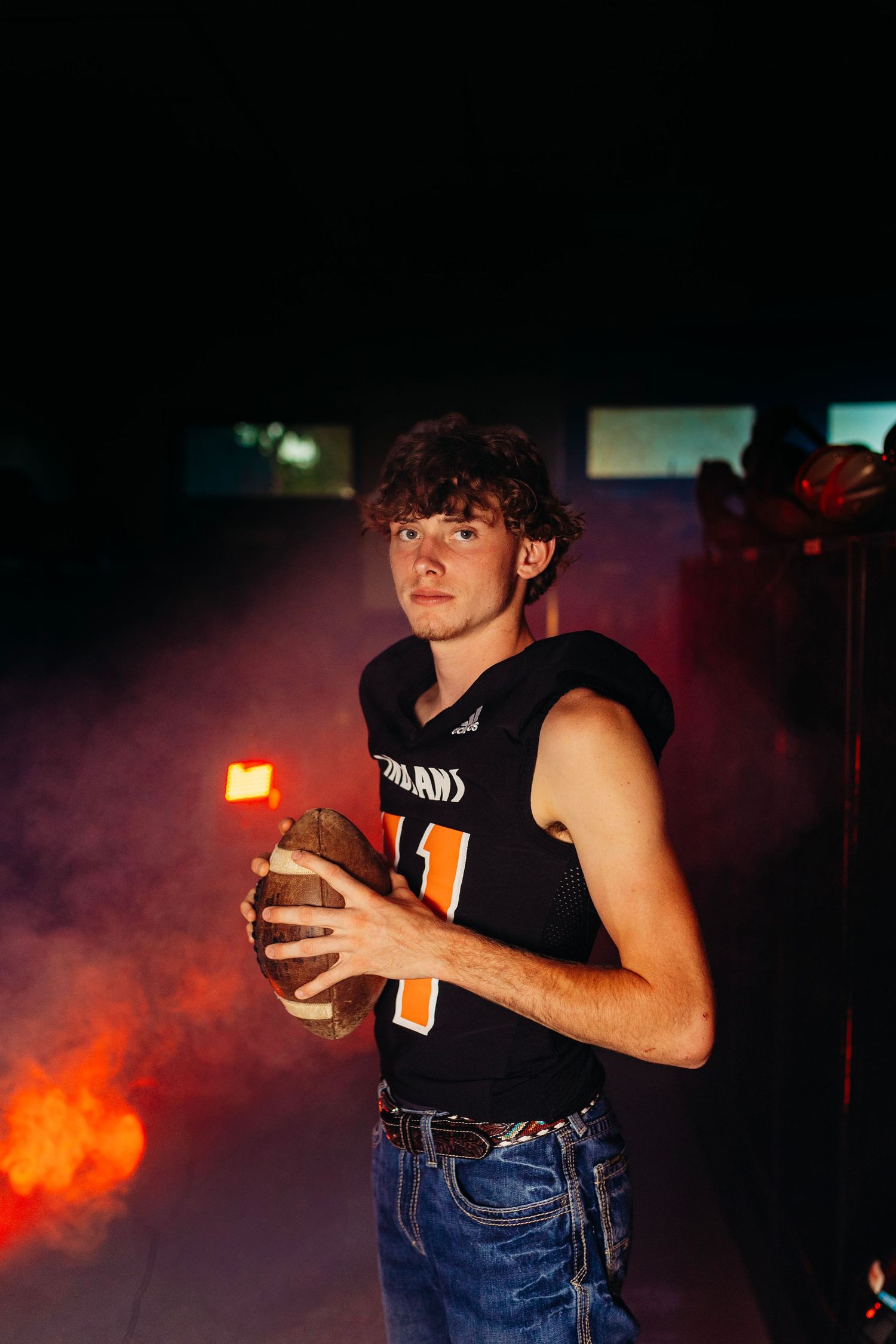 Young male football player in black jersey holding ball surrounded by dramatic smoke effect.