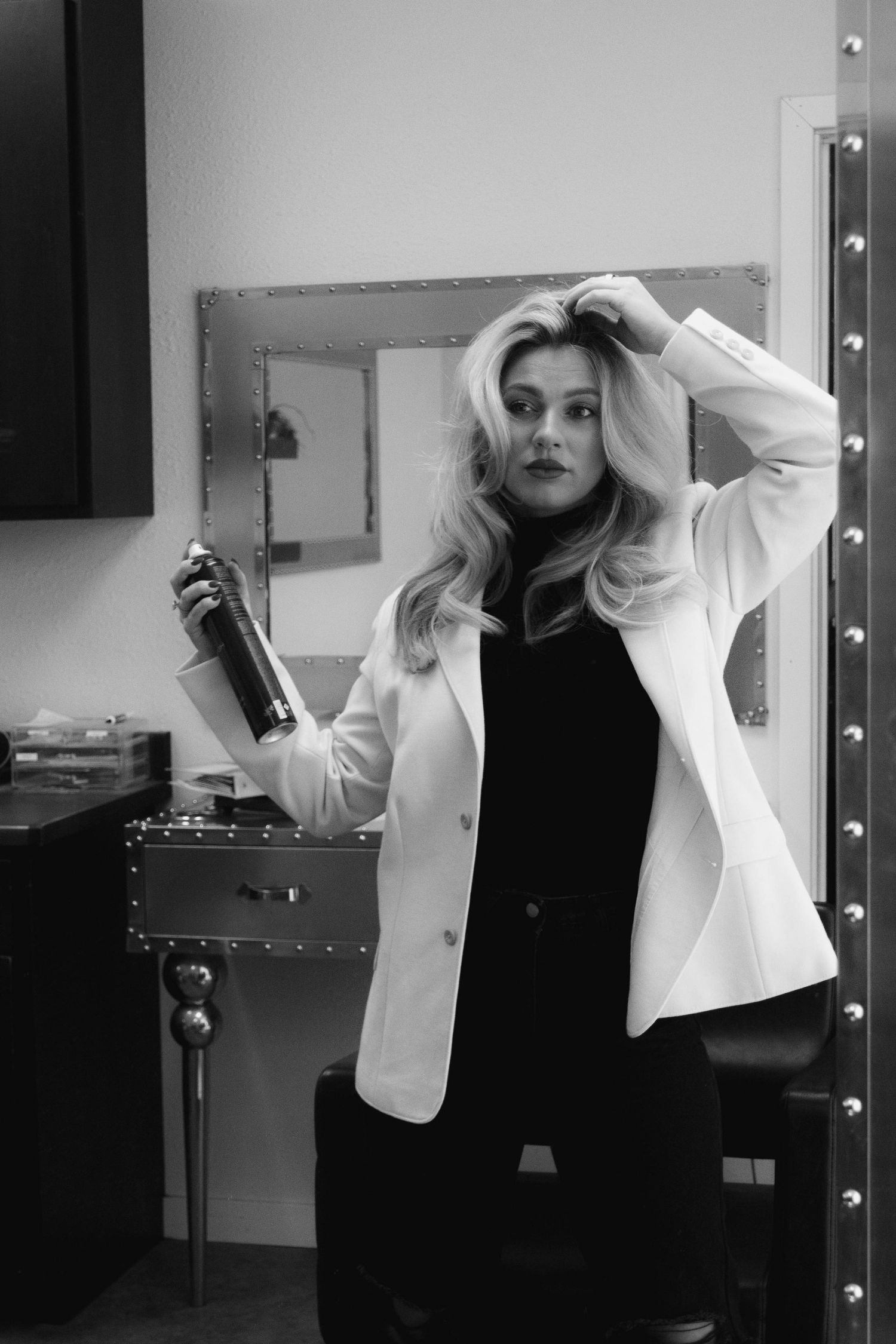 Black and white sequence of someone styling their hair in a dressing room with vanity lights.