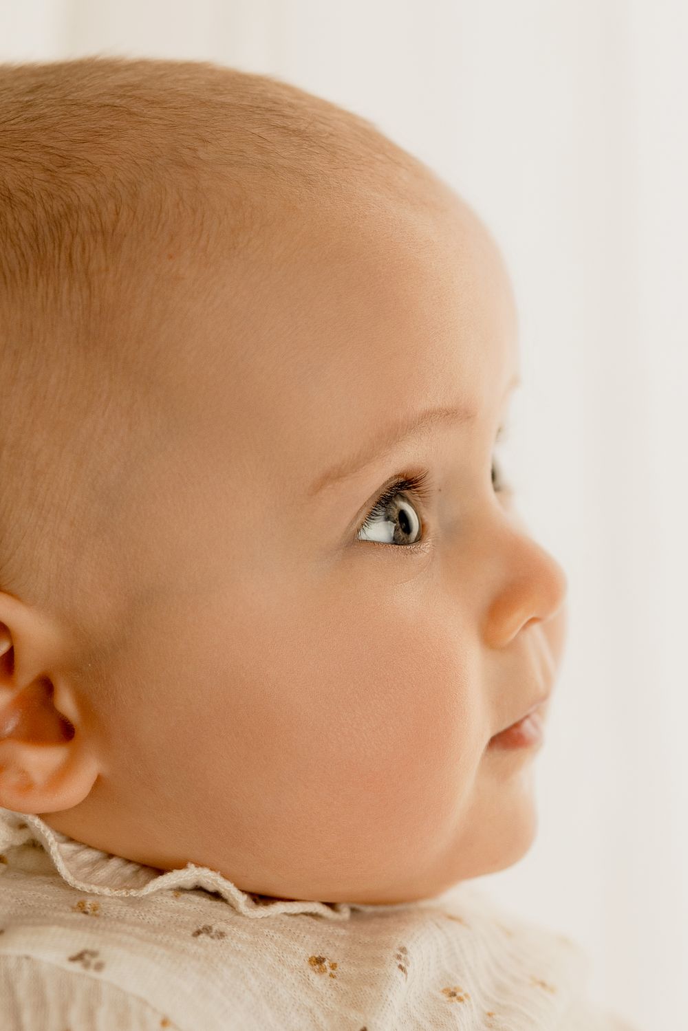 Close-up profile view of baby looking upward against white background.