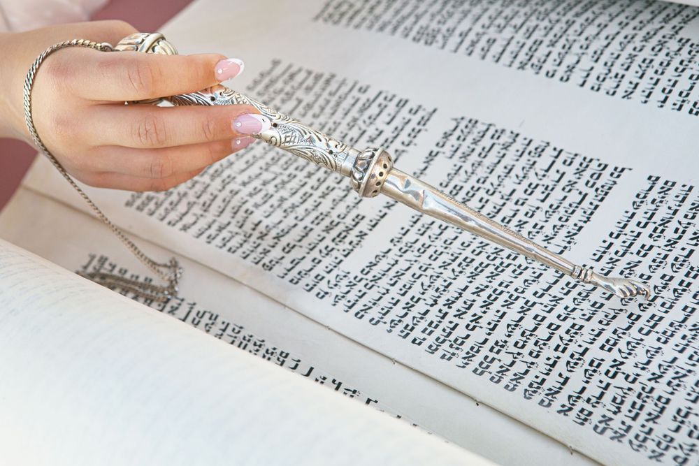 Close up photograph of a girls hand beautifully manicured holding a yad and reading the Torah.