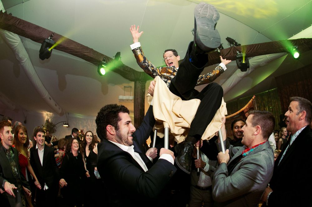 High energy wide angle photograph of a father being lifted in a chair during Bat Mitzvah Hora dance.