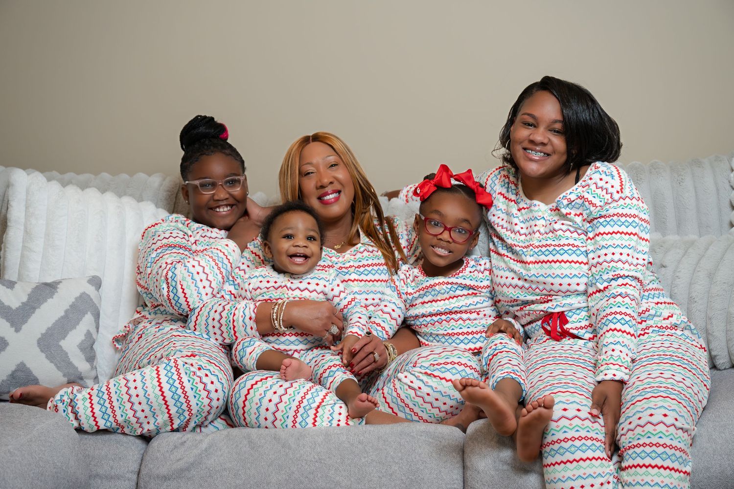 Family wearing matching striped holiday pajamas smiling together on couch.