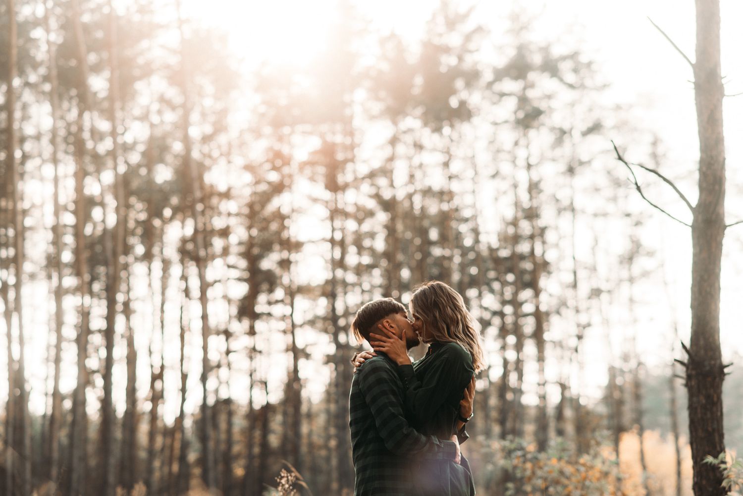 Romantic couple embracing in a sunlit forest during an Amsterdam outdoor photoshoot.