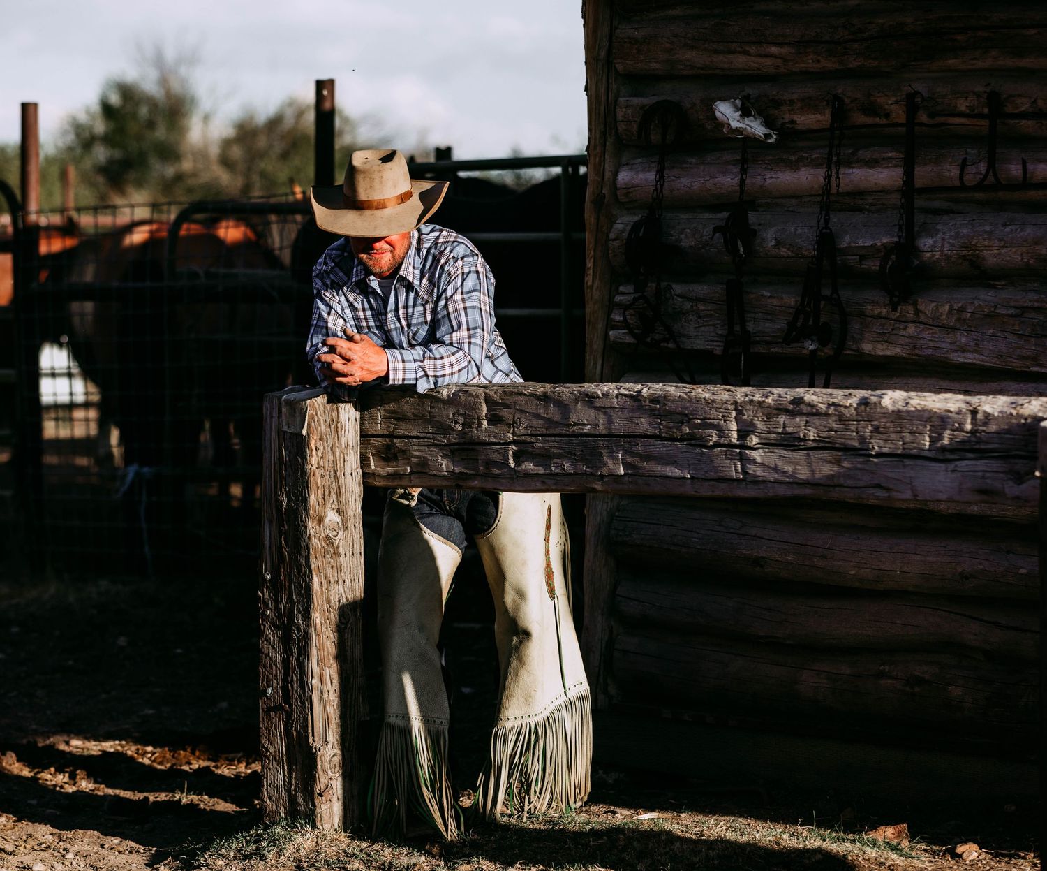 Cowboy leaning on wooden fence post in western attire.