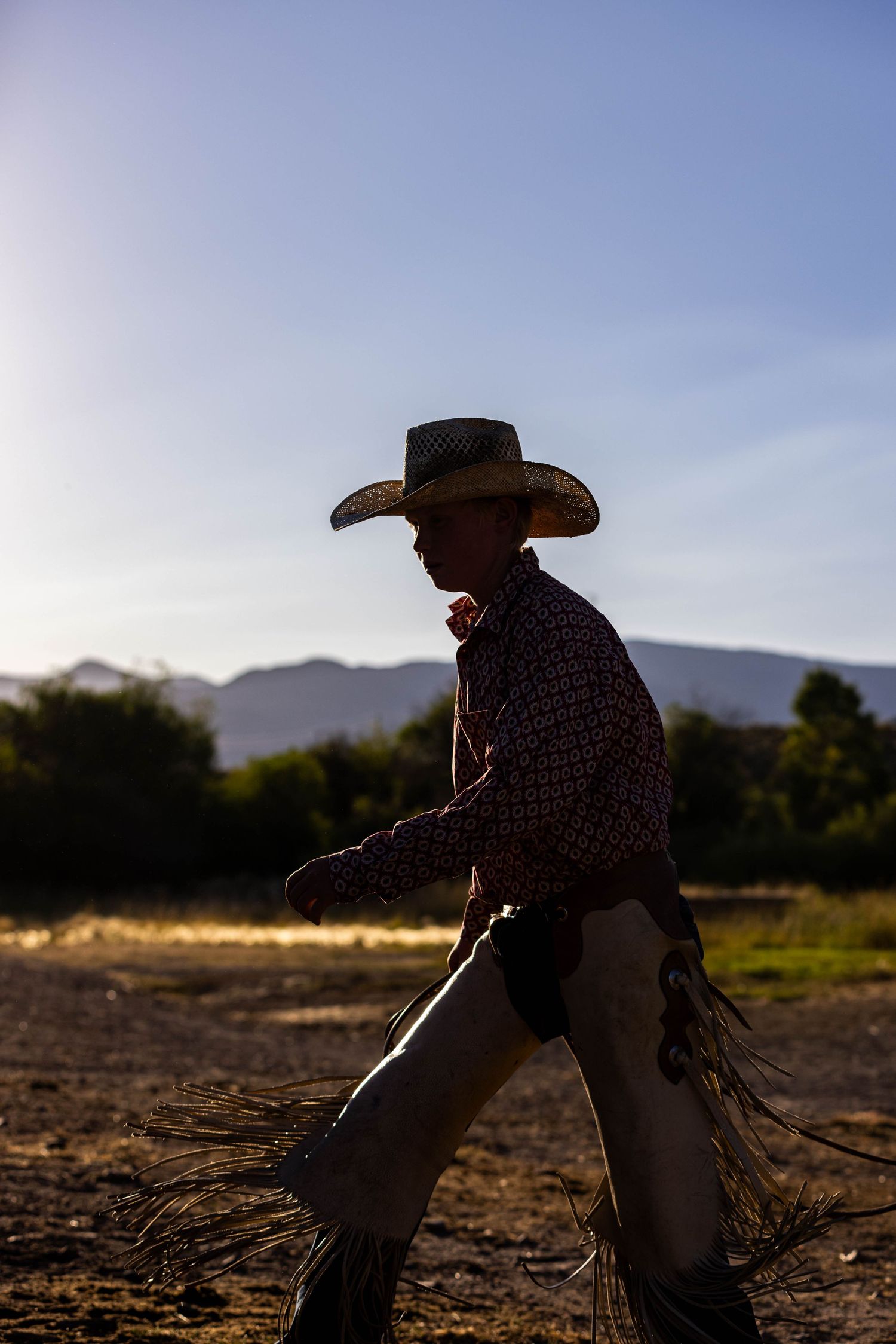 A silhouette of a cowboy walking at sunset with mountains in the background.