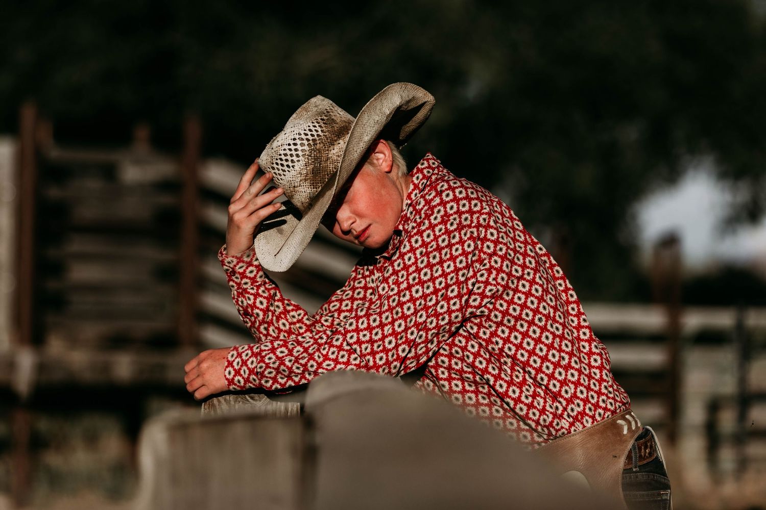 A ranch worker in a patterned shirt and cowboy hat leans forward during a ranch activity.