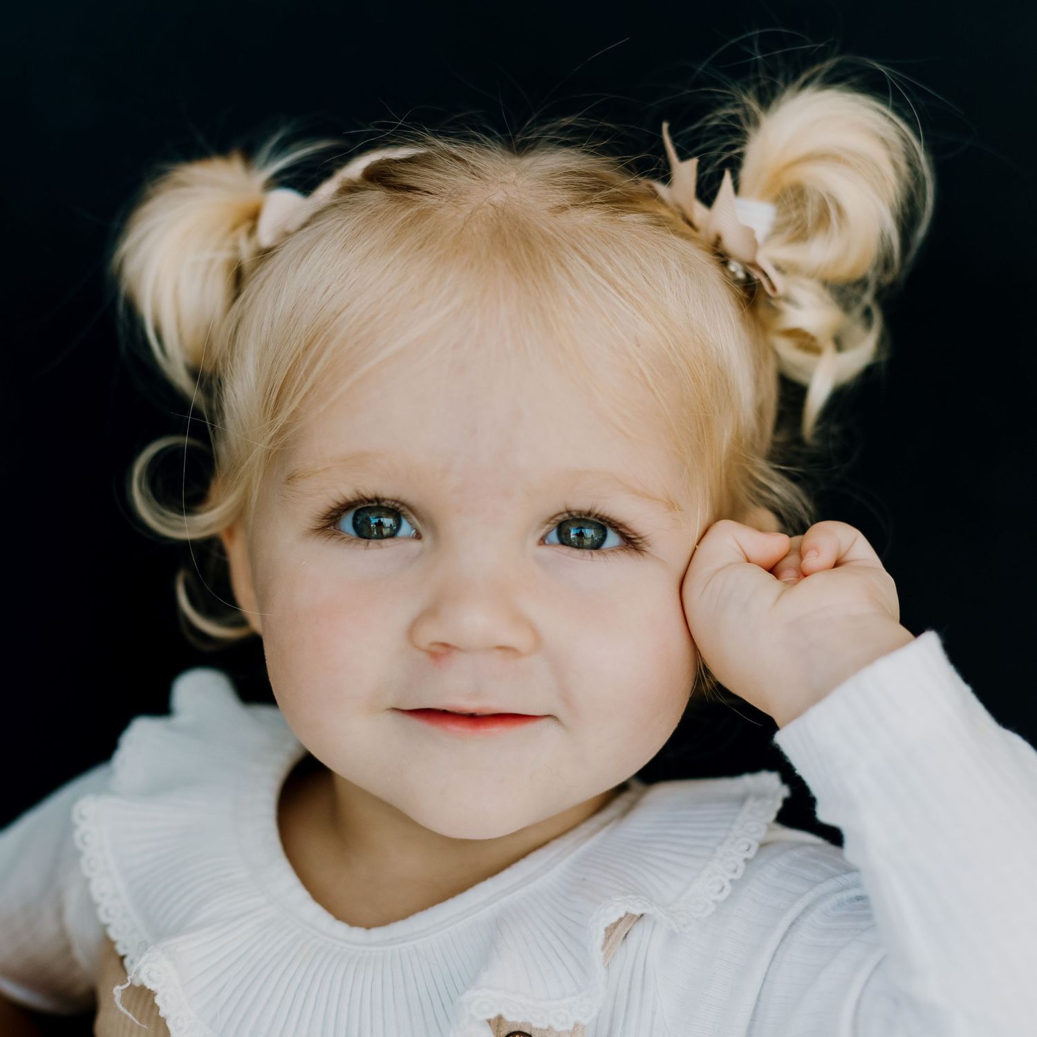 Portrait of a blonde kindergarten girl with two pigtails, looking directly at the camera during a school photography session.