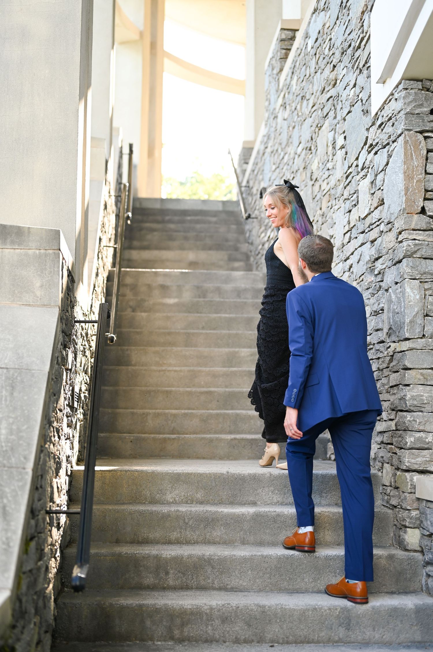 Two people ascending stone staircase with modern architecture and natural light.