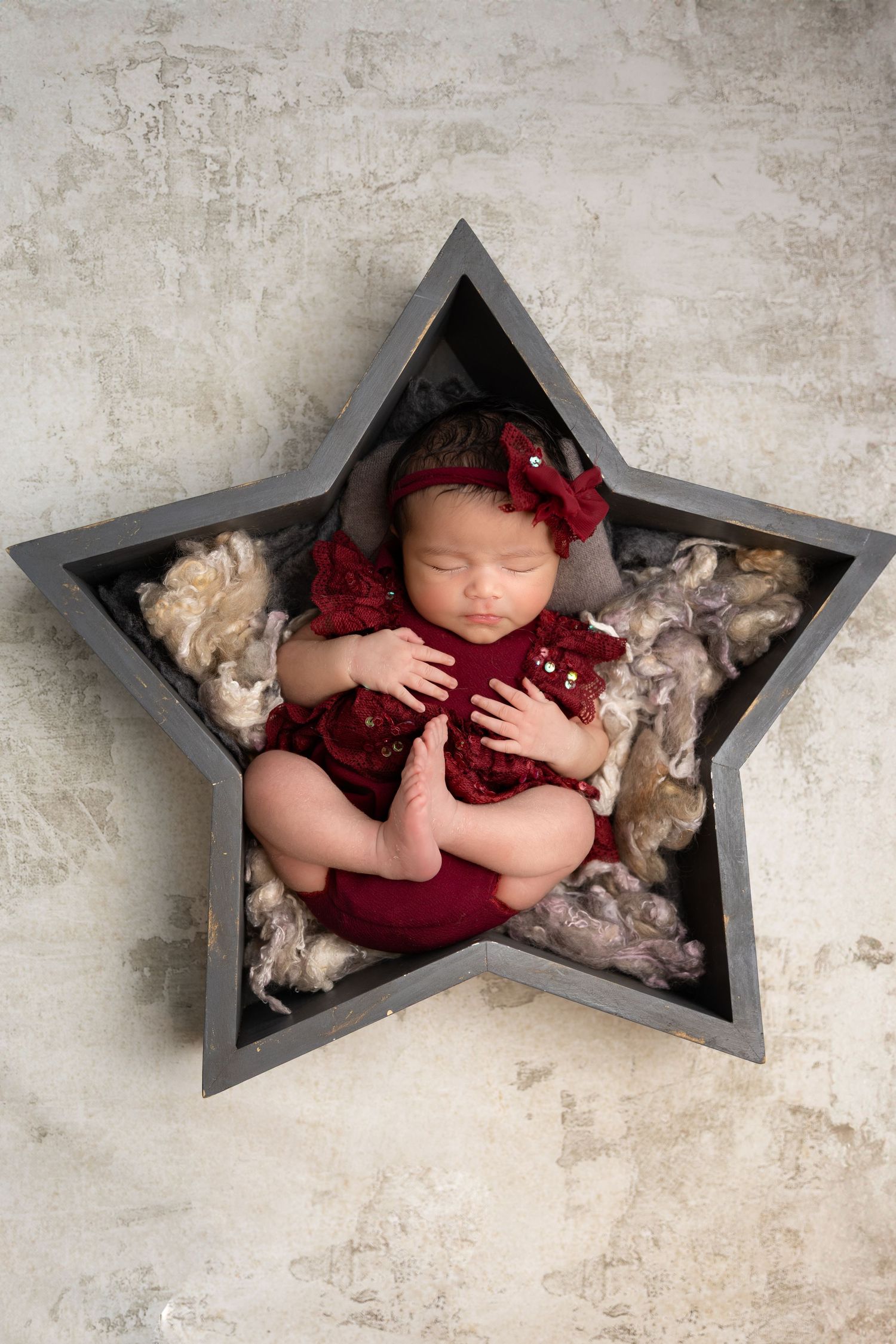 Newborn baby sleeping in a purple floral wreath swing with roses and lavender on a gray background.