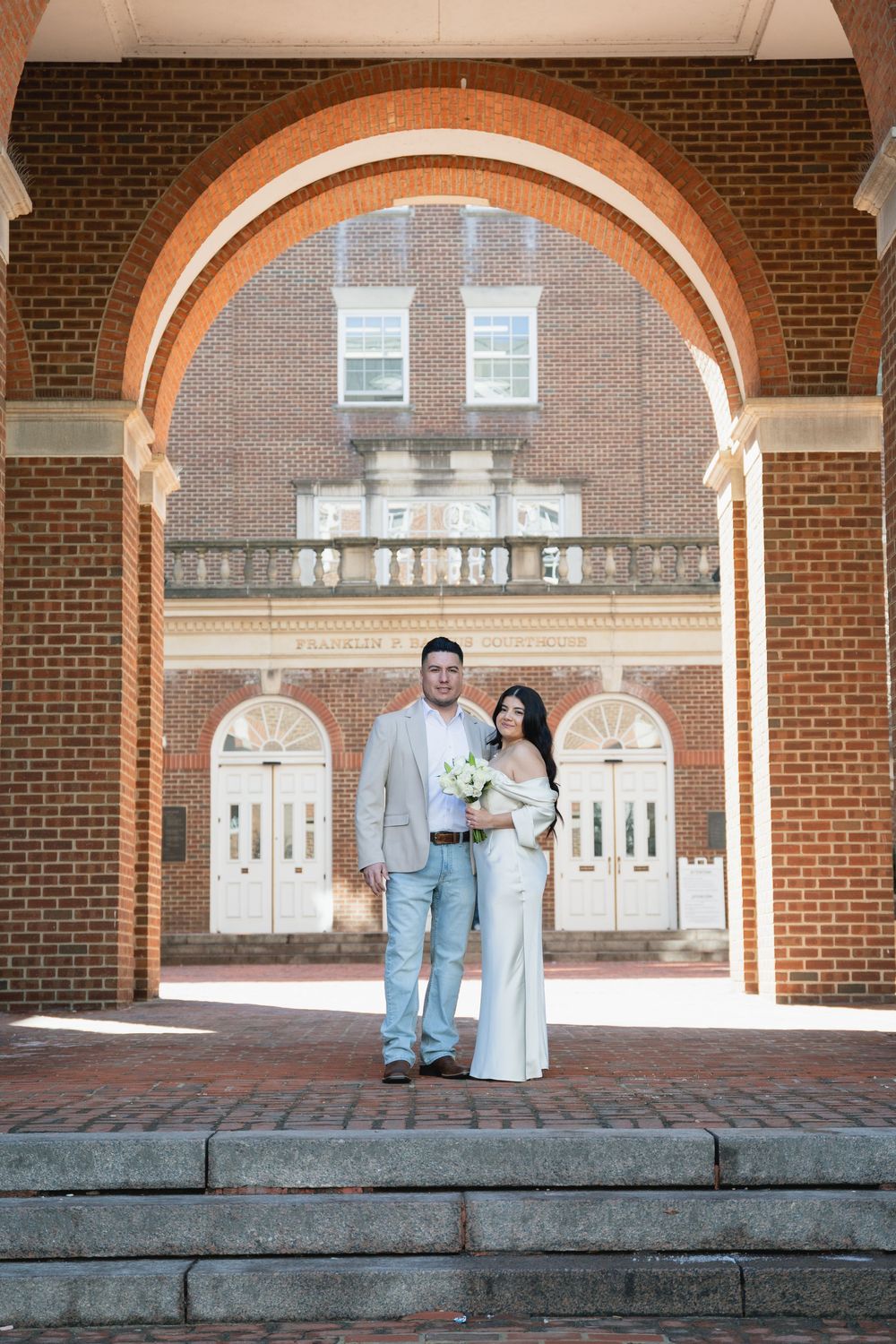 Bride and groom pose under brick arch at Franklin building on wedding day.