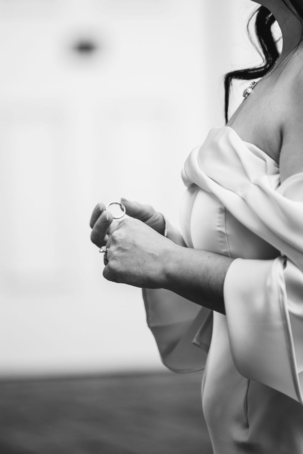 Black and white photo of a bride in a silk robe holding a delicate bracelet, preparing for her wedding day.