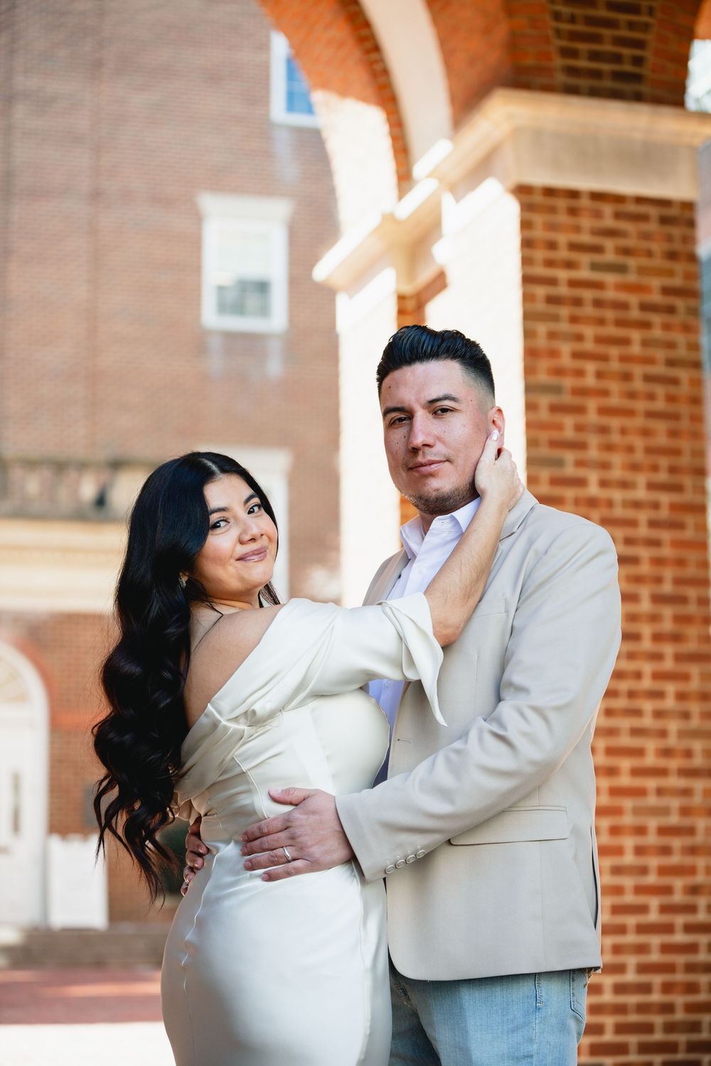 Couple posing together in wedding attire outside a brick church with a cross.
