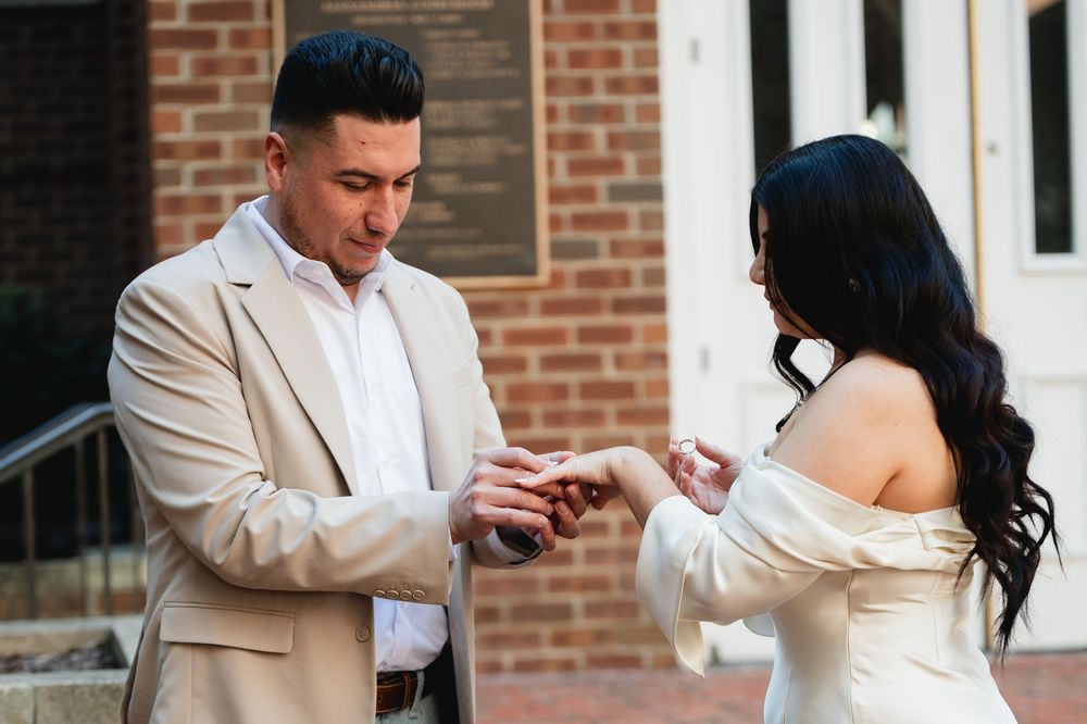 Groom placing wedding ring on bride's finger outdoors during intimate ceremony, both dressed in elegant white and beige attire.