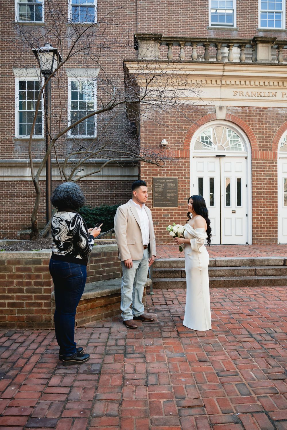 Couple exchanges vows outside Franklin building on brick plaza with officiant.