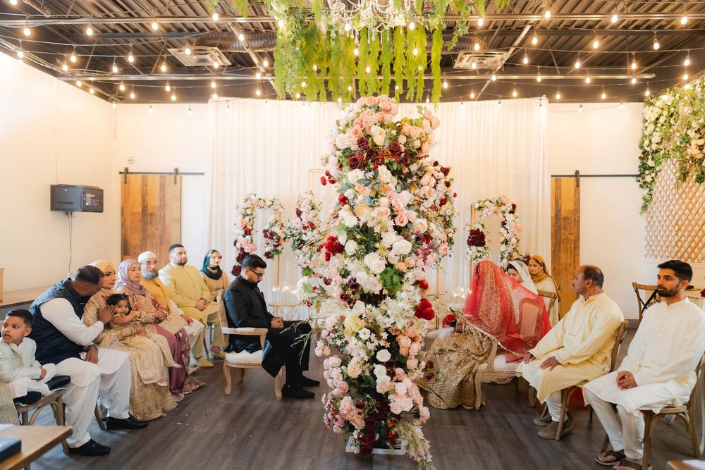 A traditional South Asian wedding ceremony with guests seated around an elaborate floral arrangement in a decorated venue.