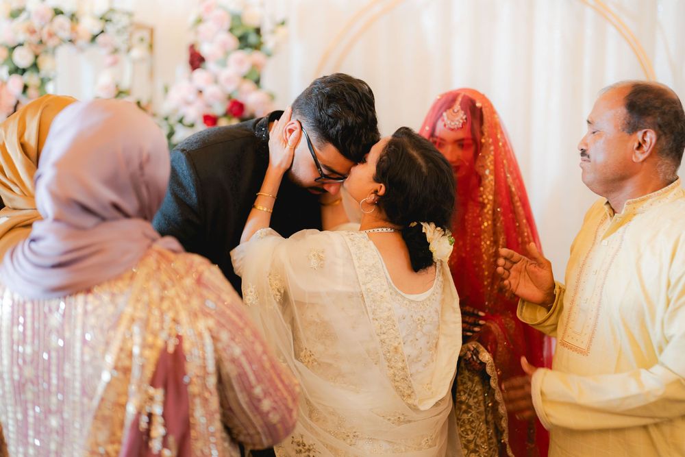 A heartfelt moment at a South Asian wedding ceremony with guests in traditional attire embracing near a floral backdrop.