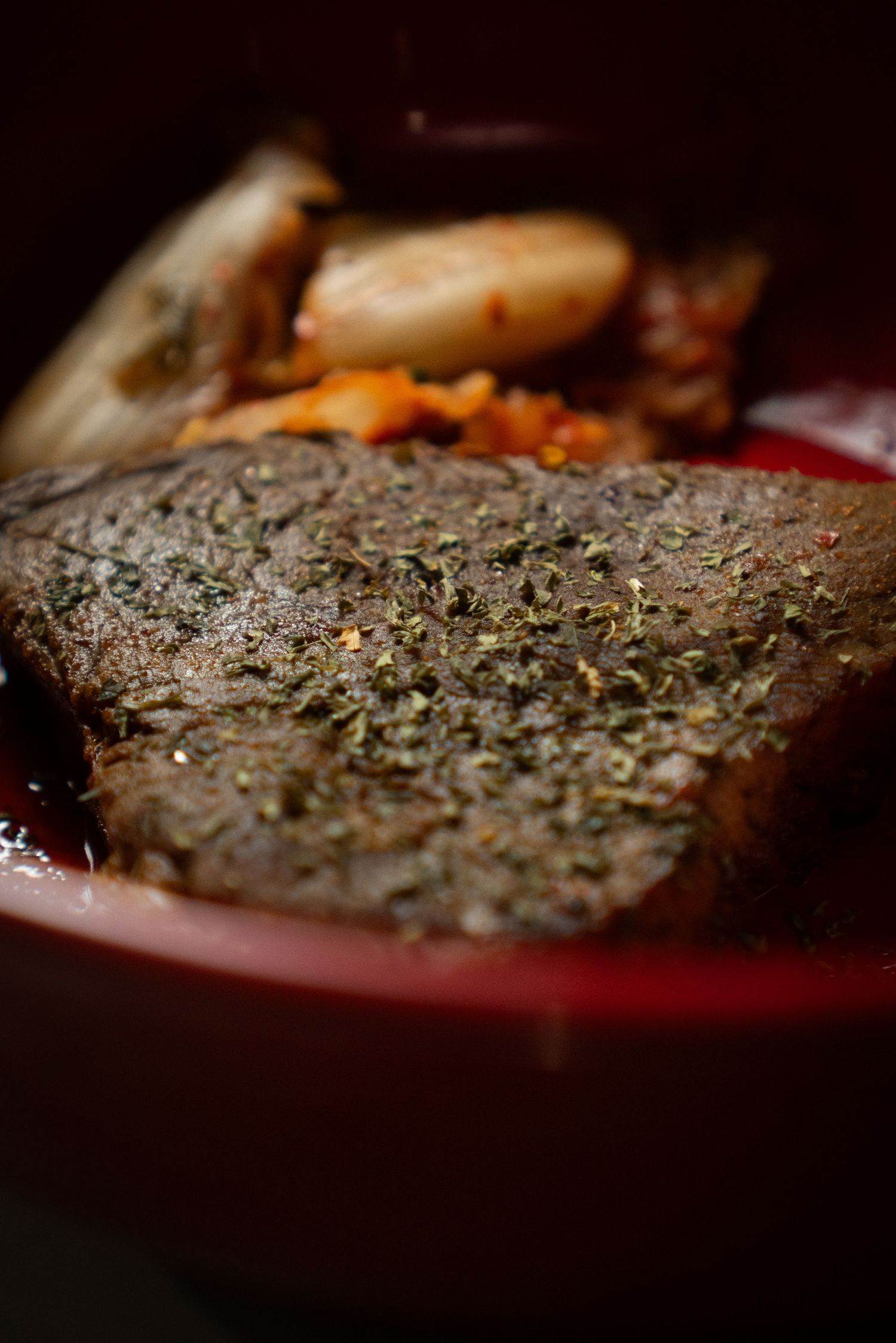 Close-up macro shot of seasoned meat with herbs and spices in dark moody lighting.