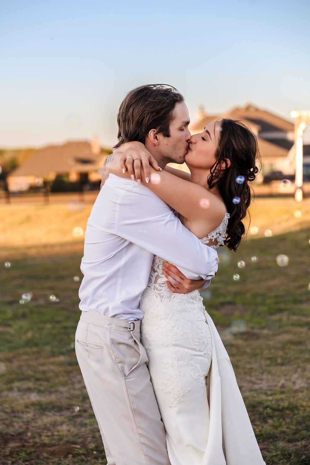 A romantic, natural light wedding portrait of a bride and groom kissing in an open field during golden hour.