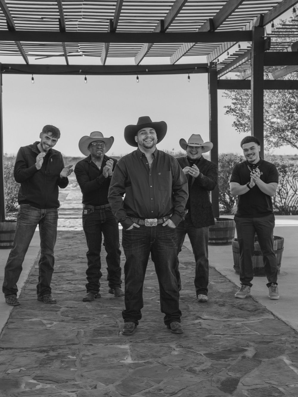 Black and white documentary-style portrait of groomsmen wearing cowboy hats standing together at a Texas wedding venue.