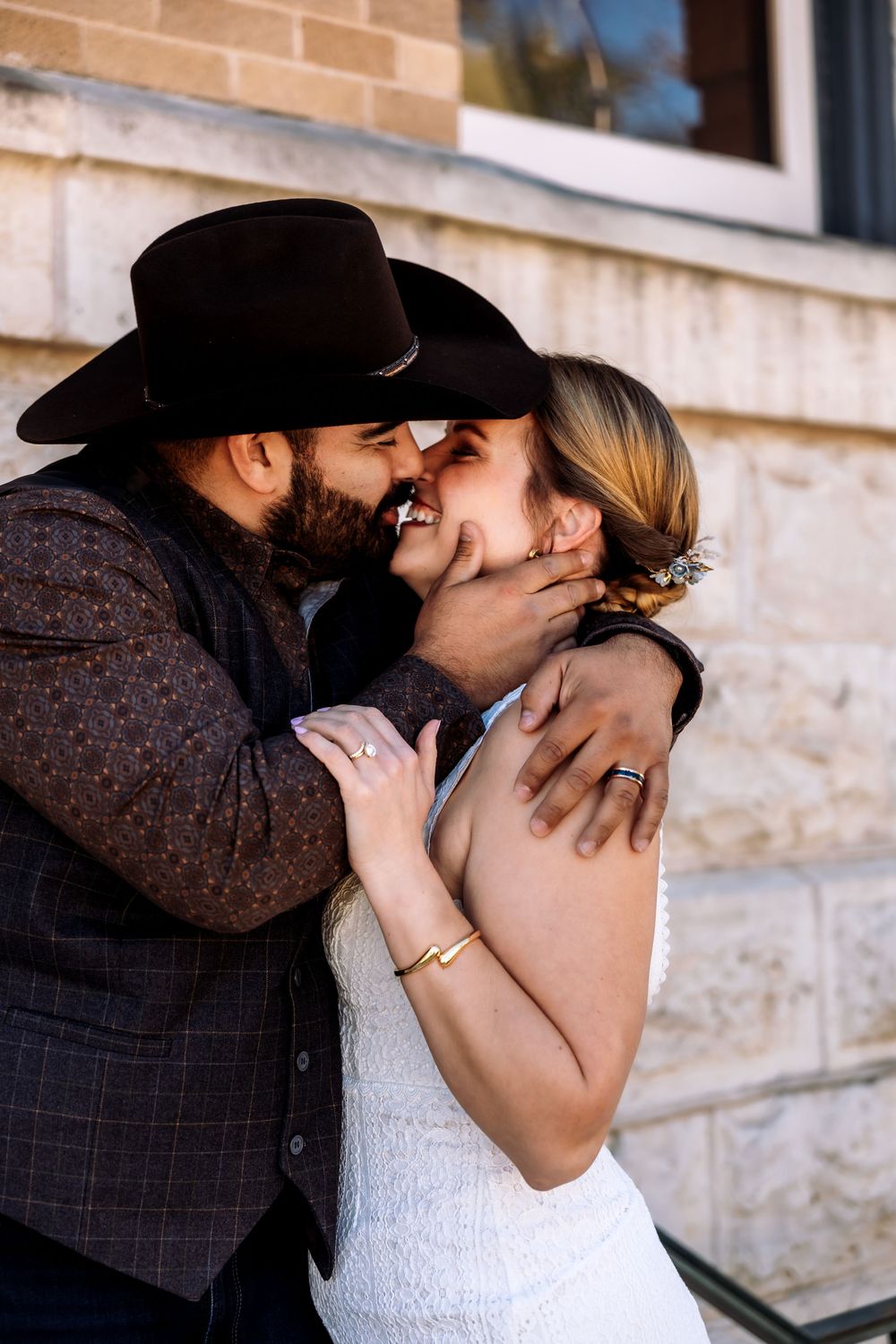Intimate outdoor wedding portrait of a bride and groom embracing, featuring a classic Texas aesthetic with a black cowboy hat.