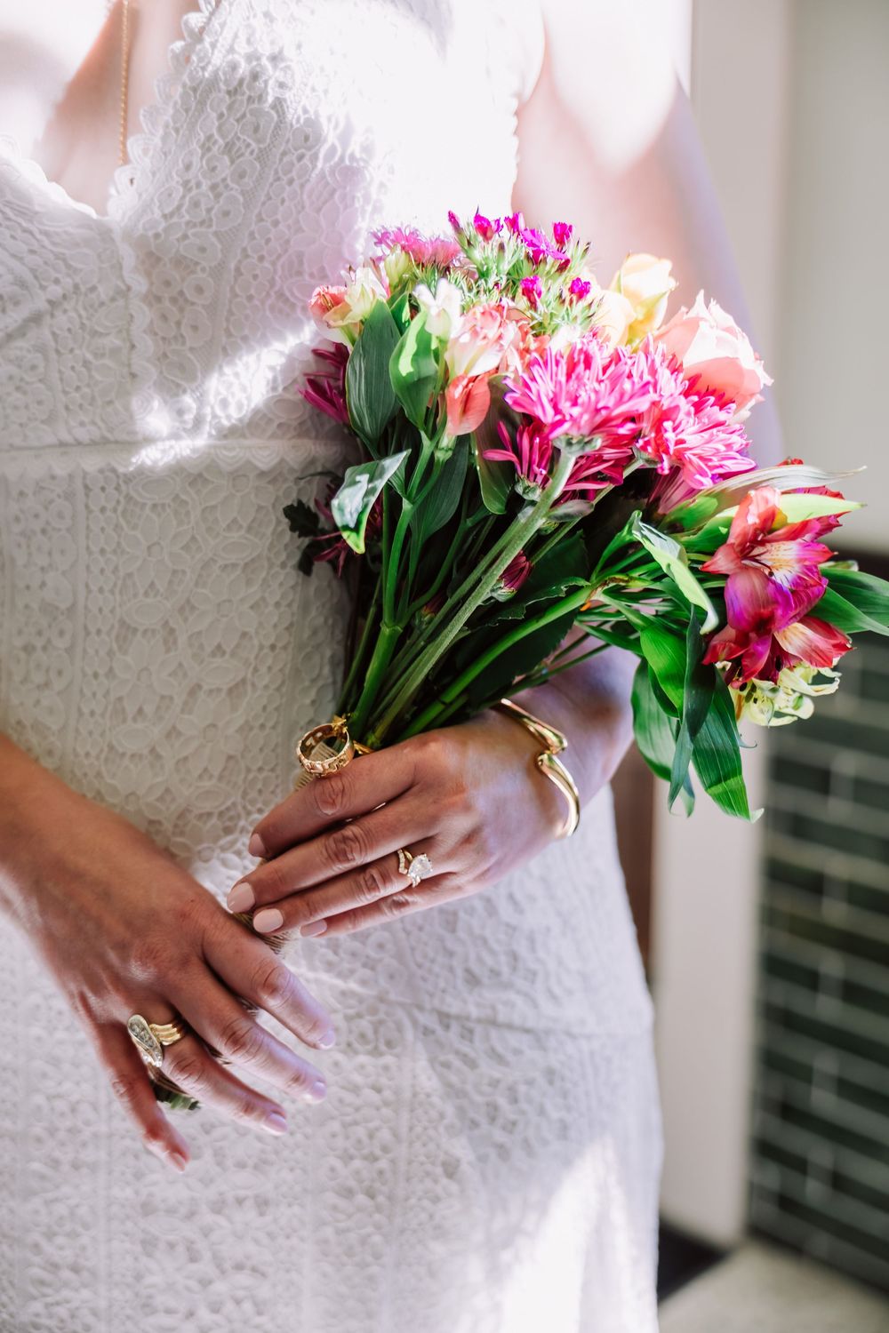 An editorial close-up of a bride holding a colorful pink and purple bouquet, focusing on the texture of her wedding gown.