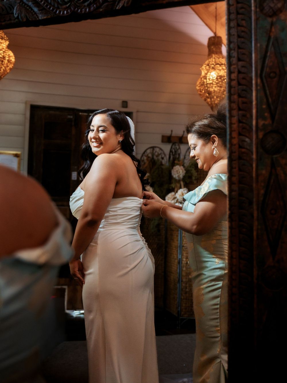 A natural light, documentary-style photo of a bride being helped into her wedding gown by her mother, capturing a quiet and genuine moment.