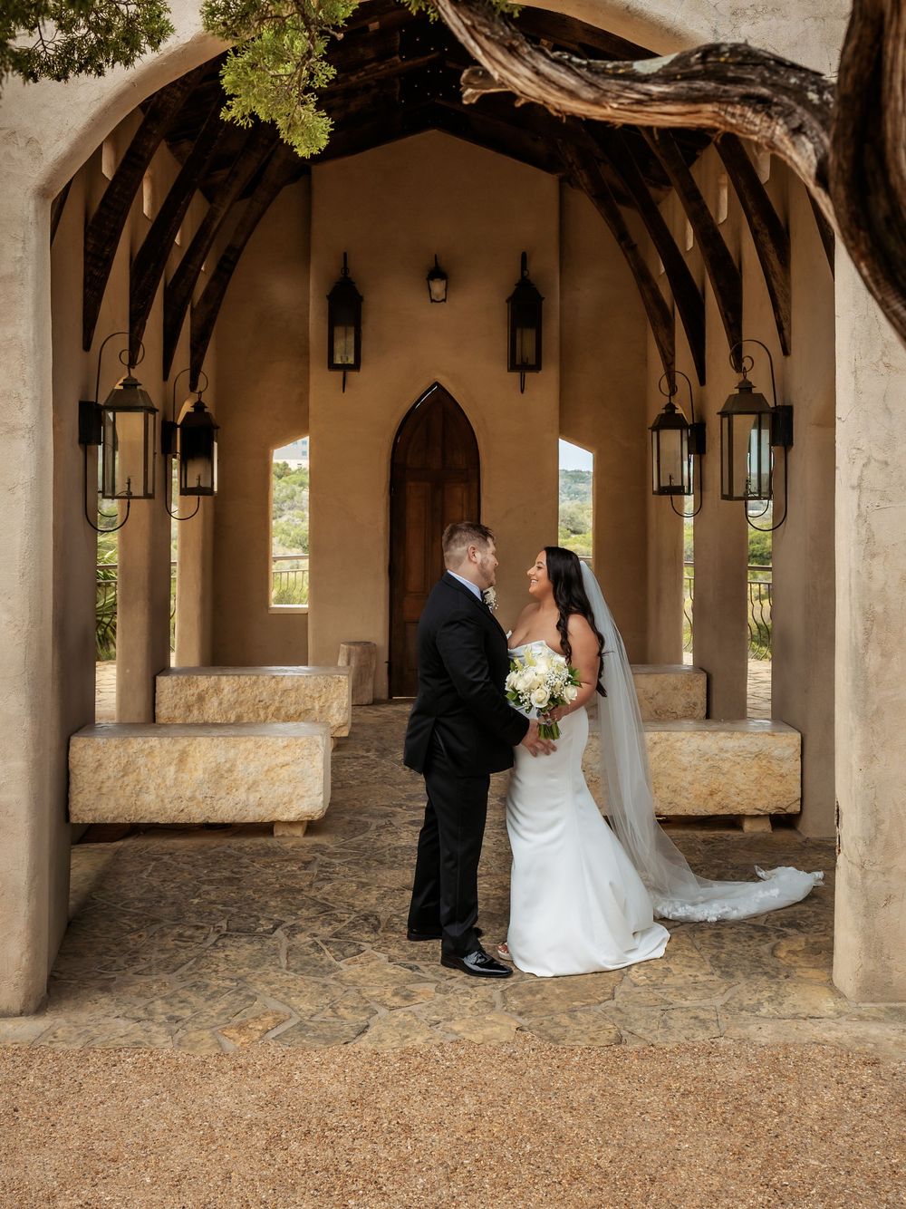 Editorial wedding portrait of a couple standing together in an elegant, sun-drenched stone archway, capturing a timeless love story.