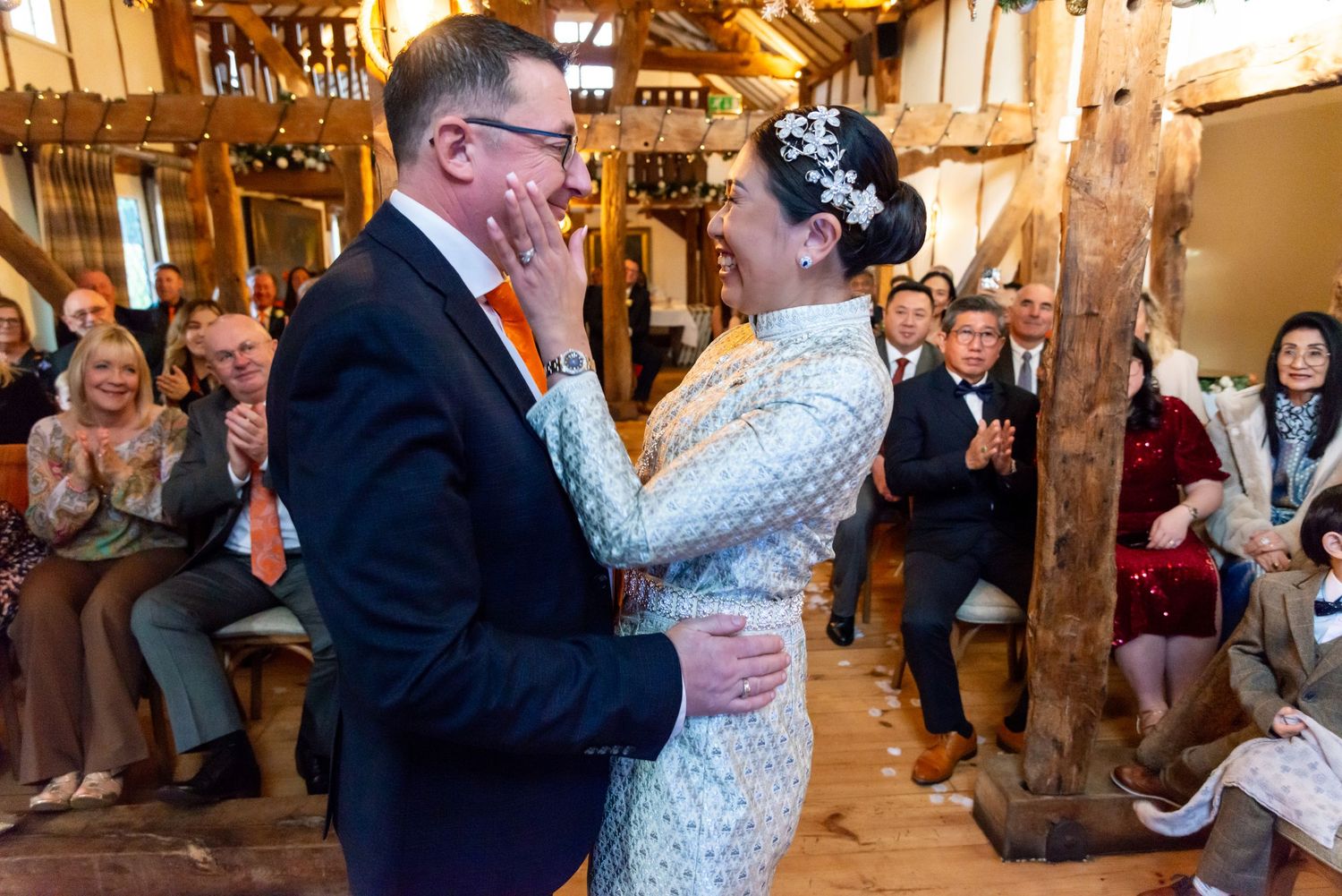 Bride and groom walking down elegant staircase, bride in white ballgown holding bouquet, groom in grey suit, grand venue.