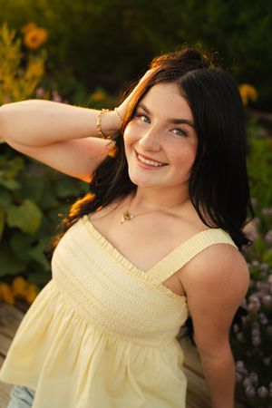 Young woman in yellow dress smiling outdoors among flowers during golden hour sunset.