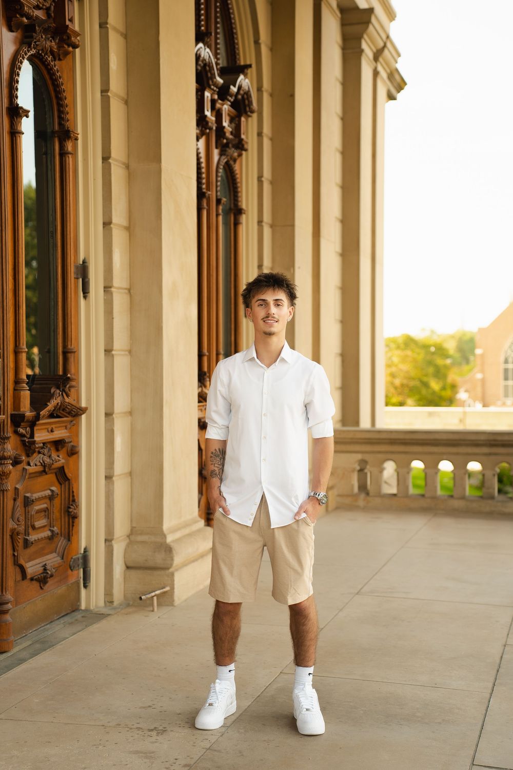 Young man in white shirt and khaki shorts standing confidently on ornate building steps.