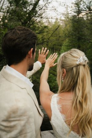 Bride and groom showing wedding rings while standing before lush green forest backdrop on their wedding day.