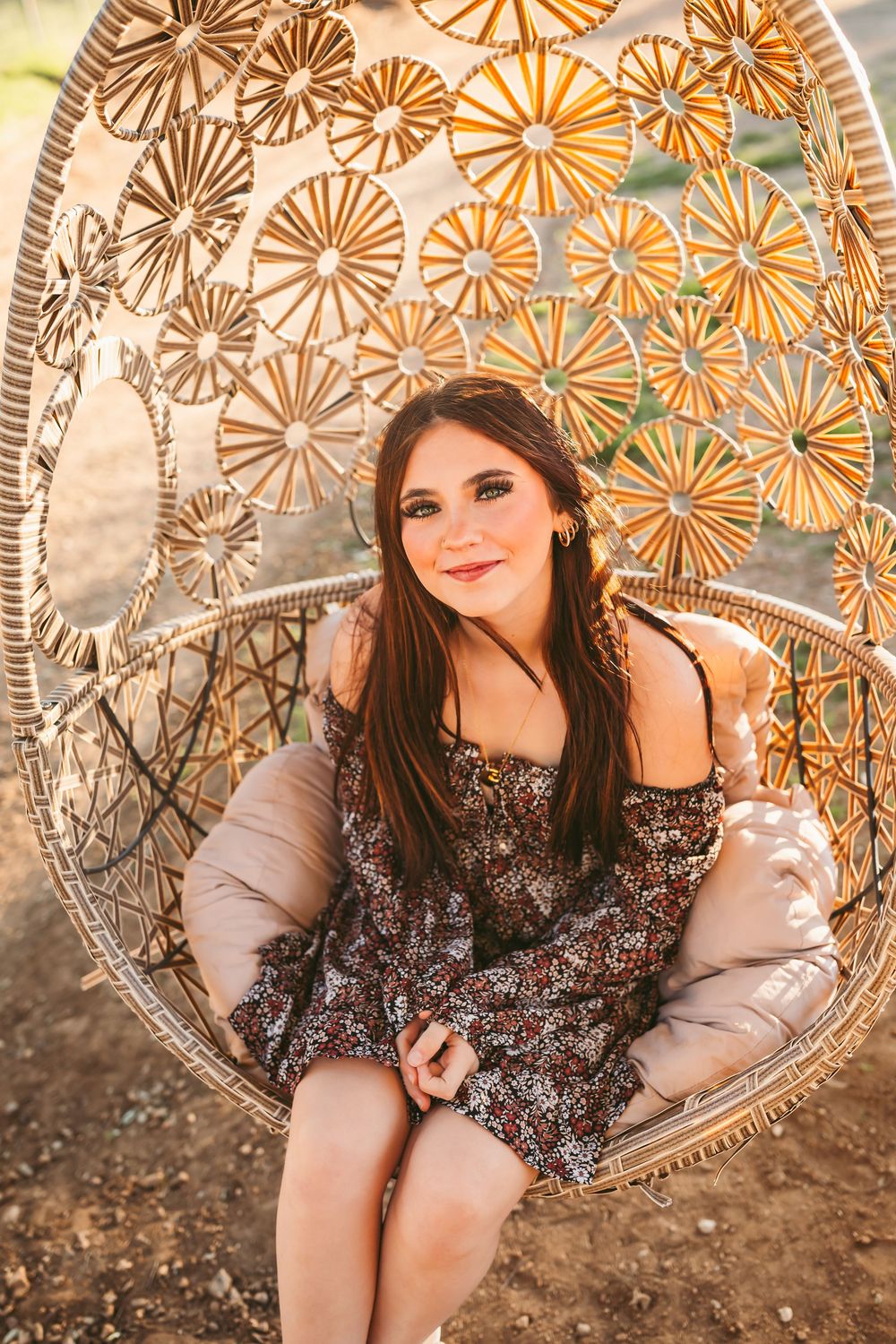 Young woman in floral dress sitting in decorative rattan egg chair outdoors in warm sunlight at blooming ridge ranch in cherry valley ca